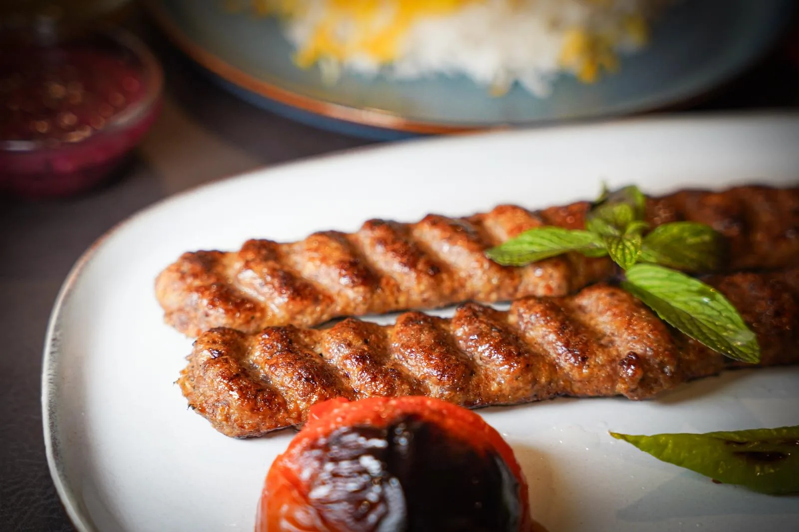 Zwei Kubideh-Spieße vom Holzkohlegrill mit gegrillter Tomate und Minze